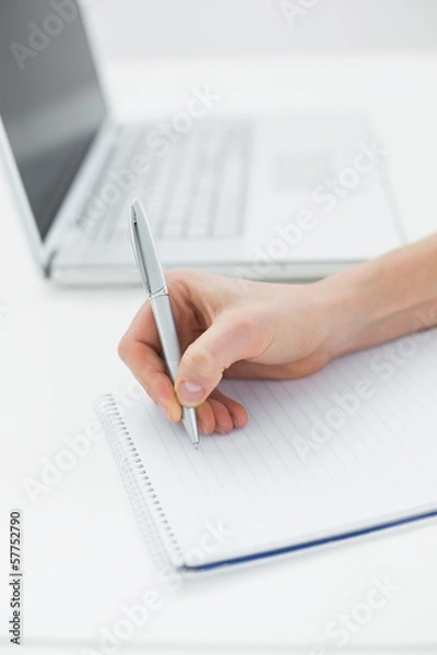 Fototapeta Close-up of a hand writing notes by laptop