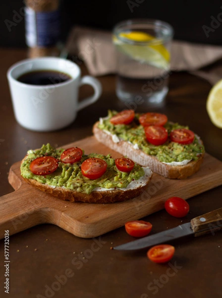Obraz Toast with avocado and cherry tomatoes on a wooden board