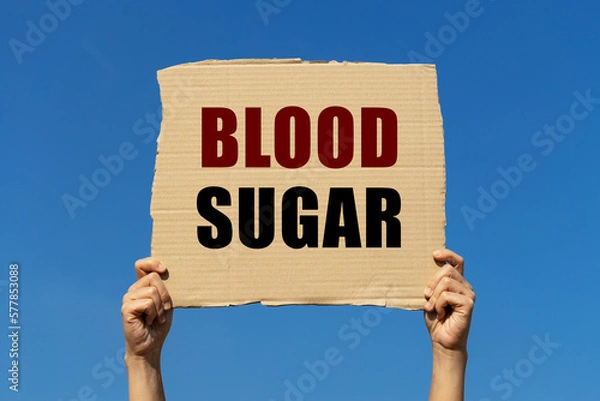 Fototapeta Blood sugar text on box paper held by 2 hands with isolated blue sky background. This message board can be used as business concept about blood sugar.