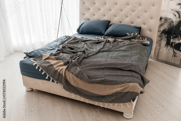 Fototapeta Unmade bed with cotton boho blanket in cozy simple bedroom. hypoallergenic Cotton bedding. concept of coziness, comfort and warmth at home