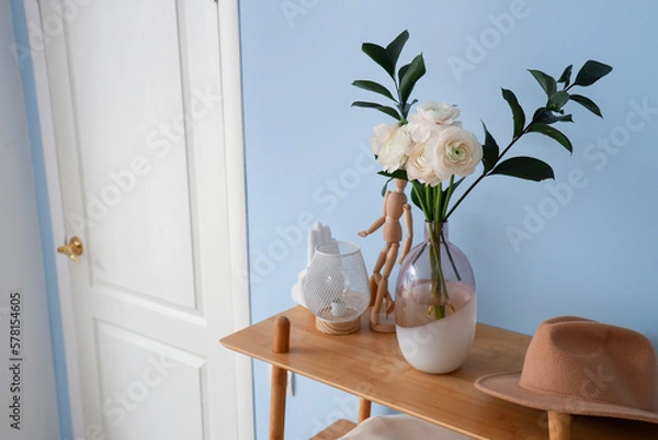 Fototapeta Vase with ranunculus flowers, mannequin, lamp and hat on shelf in hall