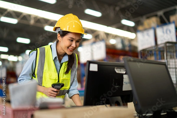 Fototapeta Asian warehouse worker Checks Stock and Inventory on Desktop Computer in retail warehouse full of shelves with goods. teamwork at warehouse storage department.