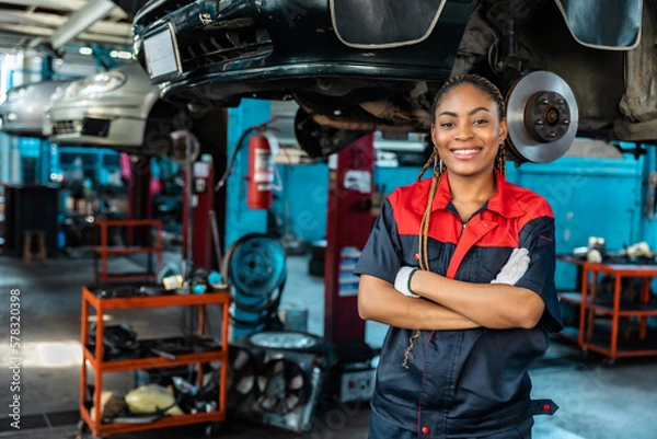 Fototapeta Engineer team checking under car condition on lifter in garage.Young auto mechanic in uniform is looking at camera and smiling examining car...
