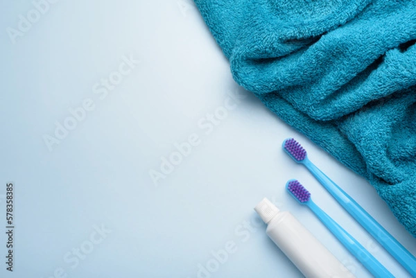 Fototapeta Toothbrushes with paste tube and towel on blue background.