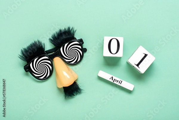 Fototapeta funny face - fake eyeglasses, nose and mustache, calendar with date 01 April on green background Happy fools day concept 1st April party Holiday greetind card
