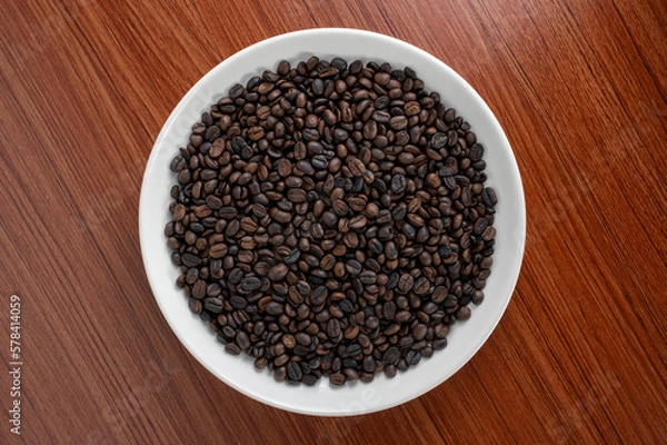 Obraz Coffee beans are placed on a plate with a wooden board in the background.  There is space for text or something.
