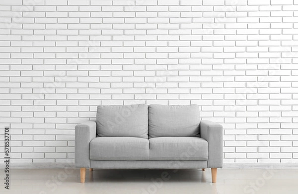 Fototapeta Stylish grey sofa near white brick wall