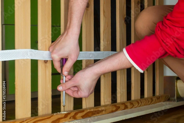 Fototapeta Screwing a screw into a wooden plank with a screwdriver
