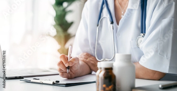 Fototapeta Doctor working on laptop computer and tablet and medical stethoscope on clipboard on desk, electronics medical record system EMRs concept.