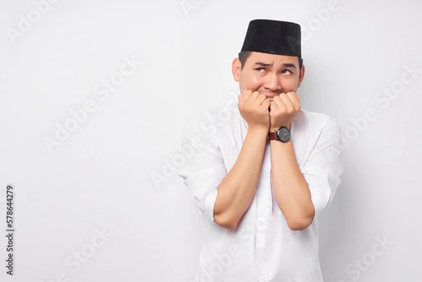 Obraz Anxiety problem. Portrait of afraid young Asian Muslim man in Arabic clothes looking stressed and nervous with hand on mouth isolated on white background. People religious Islamic lifestyle concept