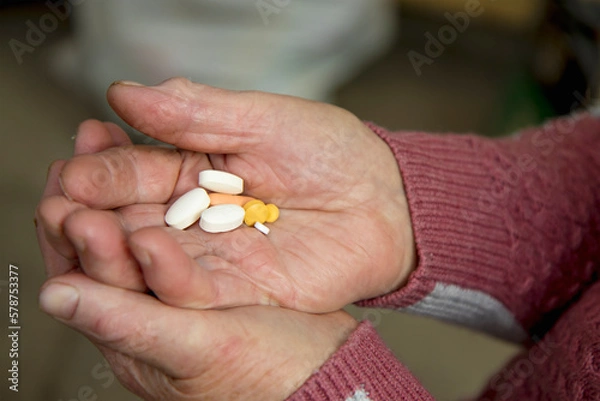 Fototapeta the hands of an elderly woman hold a handful of different pills to maintain health in old age