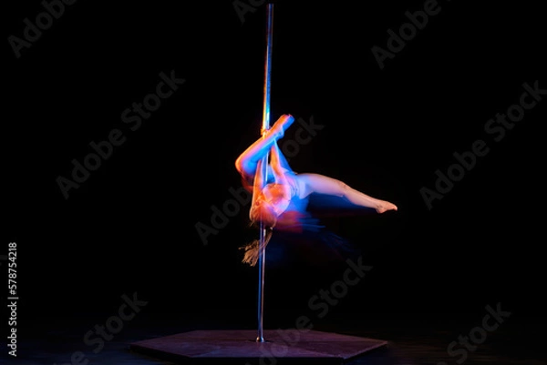 Fototapeta Passionate hobby. Young artistic girl performing pole dance isolated over black studio background with mixed neon lights. Concept of sport and dance, beauty of movements, action, modern style