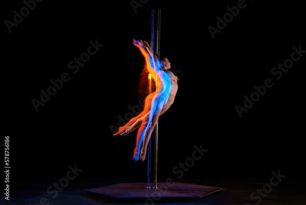 Fototapeta Gymnastic tricks. Young girl performing pole dance isolated over black studio background with mixed neon lights. Concept of sport and dance, beauty of movements, action, modern style
