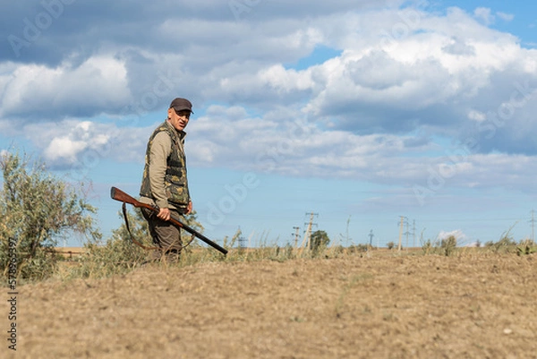 Fototapeta Mature man hunter with gun while walking on field.