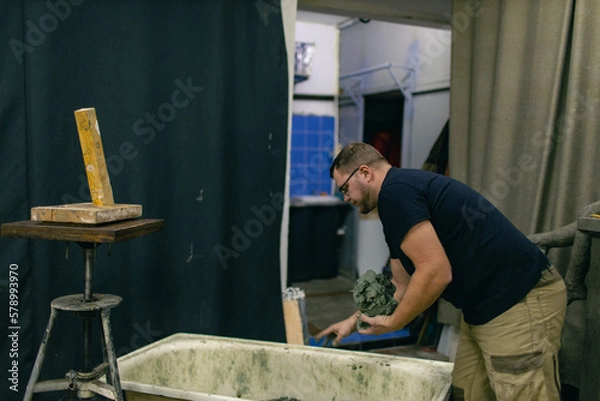 Fototapeta Man sculptor creates sculpt bust clay human woman sculpture. Statue craft creation workshop.