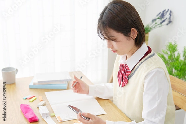 Fototapeta 家でスマホの学習アプリを使って勉強する女子高生