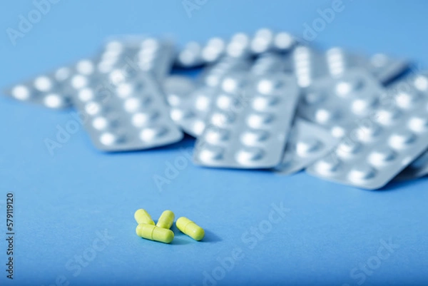 Fototapeta Yellow capsules and different blister of pills. Different pills. Medical and different concept of light blue paper background with copy space.
