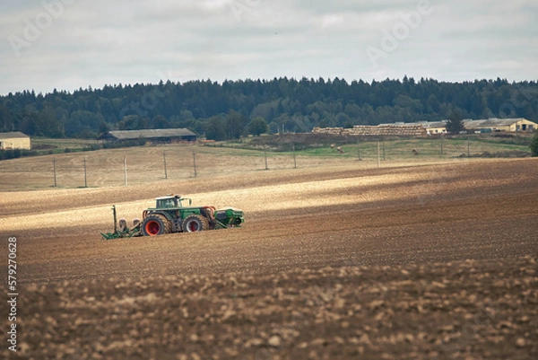 Fototapeta Tractor with seeder at work in field. Tractor with seed drill and power harrow working on field. Farmer driving tractor and drilling seed in ploughed field. Farmer seeding, sowing crops at field