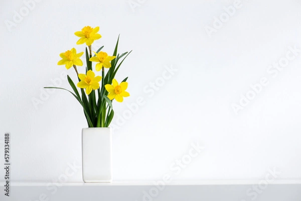 Obraz Hello summer background concept. Beautiful yellow bunch of blossoming narcissus flowers in white vase on white nature background, space for text.