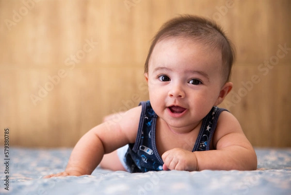 Fototapeta baby lying on a bed, looking forward and smiling.