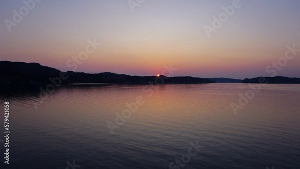 Fototapeta Colorful sunset over a lake, bits of land and mountains in the background