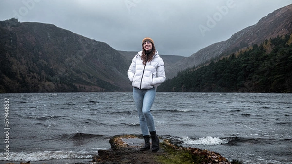Obraz Woman standing on a piece of land in front of a lake during stormy weather in the mountains