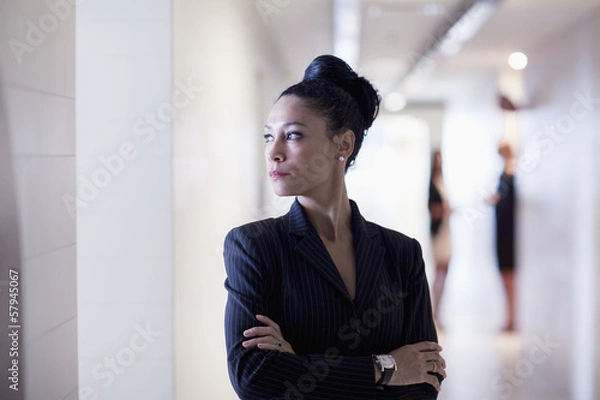 Fototapeta Businesswoman standing in the corridor with arms crossed looking away