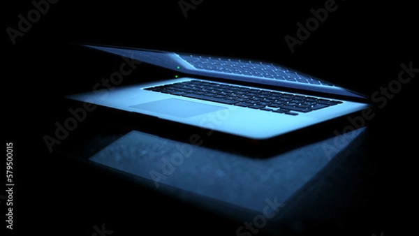 Fototapeta Laptop on a black background. Slightly open laptop. The computer screen lights up, the keyboard lights up