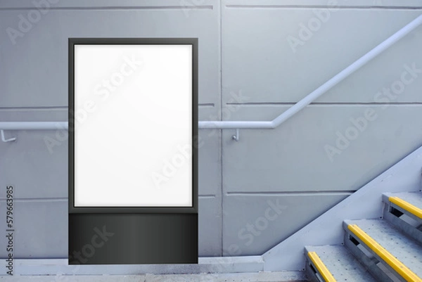 Fototapeta Blank white vertical digital display in front of painted concrete wall, beside flight of stairs. Template for mock up of advertising poster