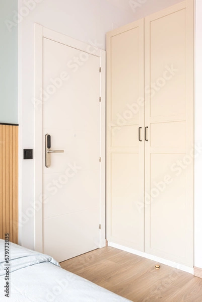 Fototapeta View of white front doors with electronic digital lock next to wardrobe and bed in hotel room. Concept of a modern security and protection system
