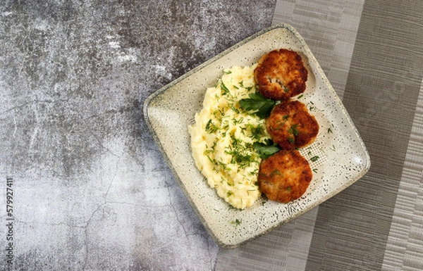 Fototapeta Mashed potatoes with cutlets and herbs on a square  plate on a dark background. Top view, flat lay