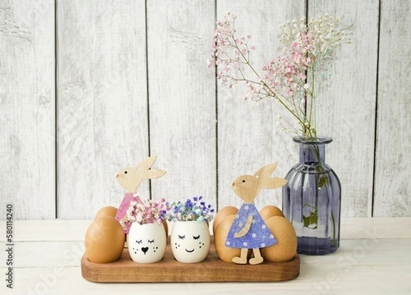 Obraz On a wooden background, a festive Easter composition, home office decorations, Easter eggs decorated with flowers and cute wooden rabbits.  Easter holiday concept, front view, background.