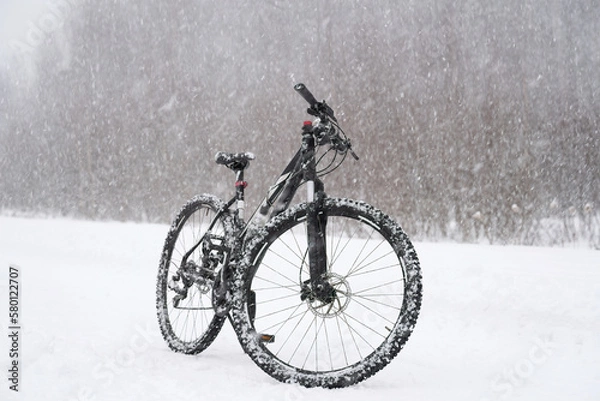 Fototapeta A black bicycle on a snowy road in the forest during a heavy snowfall in winter