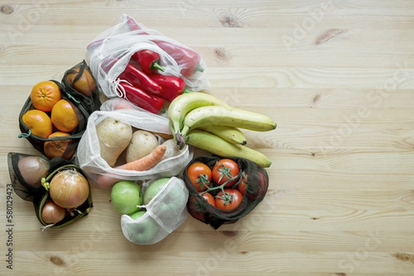 Fototapeta Vegetables and fruits in reusable shopping bags on a wooden table. The concept of zero waste and eco-friendly lifestyle. No plastic. Top view.