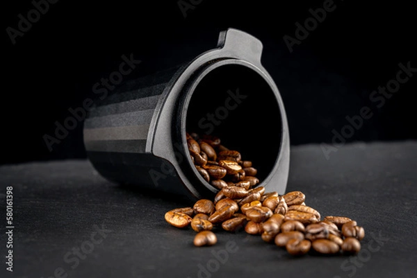 Obraz Dosing cup with black matte texture. Top view on black background with coffee beans. Barista tool for dosing coffee beans and using it to when grinding beans. Focus on the beans in the center..