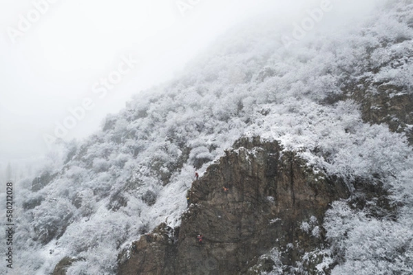 Fototapeta Aerial shot of snow covered cliffs conquered by climbers