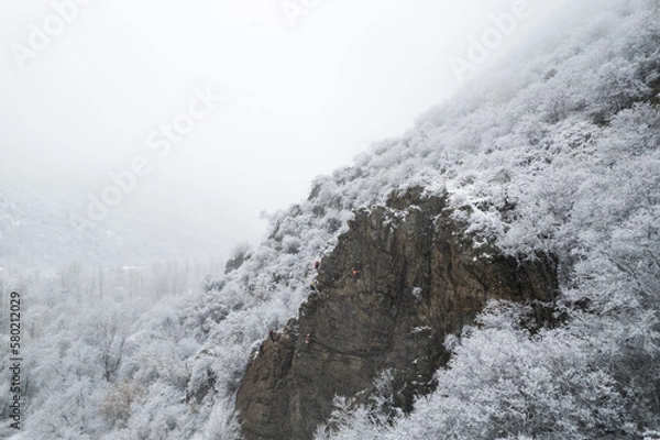 Fototapeta Aerial shot of snow covered cliffs conquered by climbers