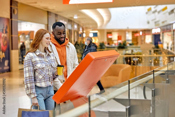 Obraz happy cheerful diverse family at the information kiosk in the mall as an interactive customer service. couple using navigator while doing shopping in Hypermarket, technology, side view photo