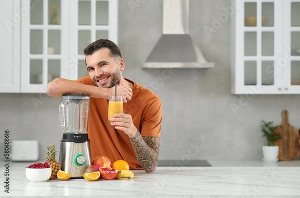 Fototapeta Handsome man with delicious smoothie at white marble table in kitchen. Space for text