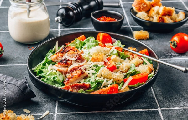 Fototapeta Homemade Caesar salad with crispy chicken and tomatoes on a black tiled background