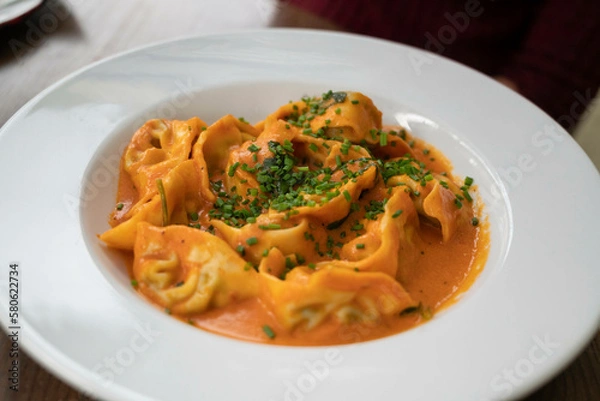 Fototapeta Ricotta and spinach ravioli in rose sauce, garnished with chives, served in a deep plate
