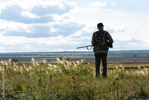 Fototapeta Mature man hunter with gun while walking on field.