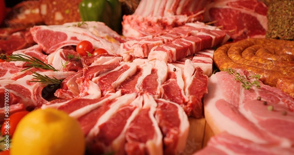 Fototapeta Meat products on display for sale on butchers table. Layout of various sausages and raw meat chunks. Handmade meat goods concept.