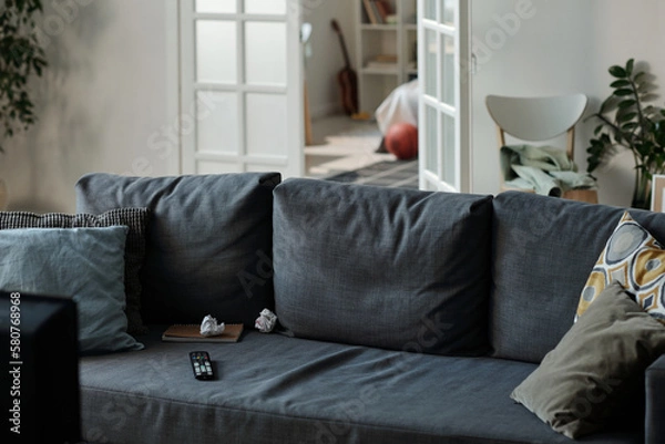 Fototapeta Grey comfortable couch with several soft pillows standing in the center of living room against open door and part of cozy bedroom