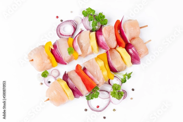 Obraz Raw pieces of chicken skewers with pepper onion and pineapple on a white background.Uncooked mixed meat skewer with peppers.Skewers with pieces of raw meat, red, yellow and green pepper.Top view.