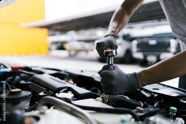 Fototapeta Professional car mechanic using a wrench for working on the engine of the car in the garage for car auto repair service and maintenance check concept for the car before leaving.