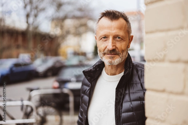 Fototapeta A mature adult, smiling with happiness while looking at the camera in a city portrait, his gray hair and beard adding to his character.
