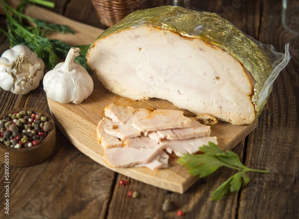 Fototapeta homemade boiled pork whole and sliced, smoked lies on a wooden cutting vintage board on a rustic background.boiled pork