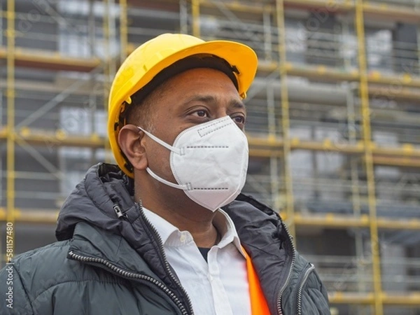 Obraz Indian construction worker wearing a safety helmet and a protective ffp2 mask posing on construction site