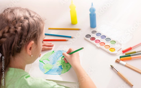 Fototapeta A girl draws the planet Earth on a sheet of paper with a colored pencil